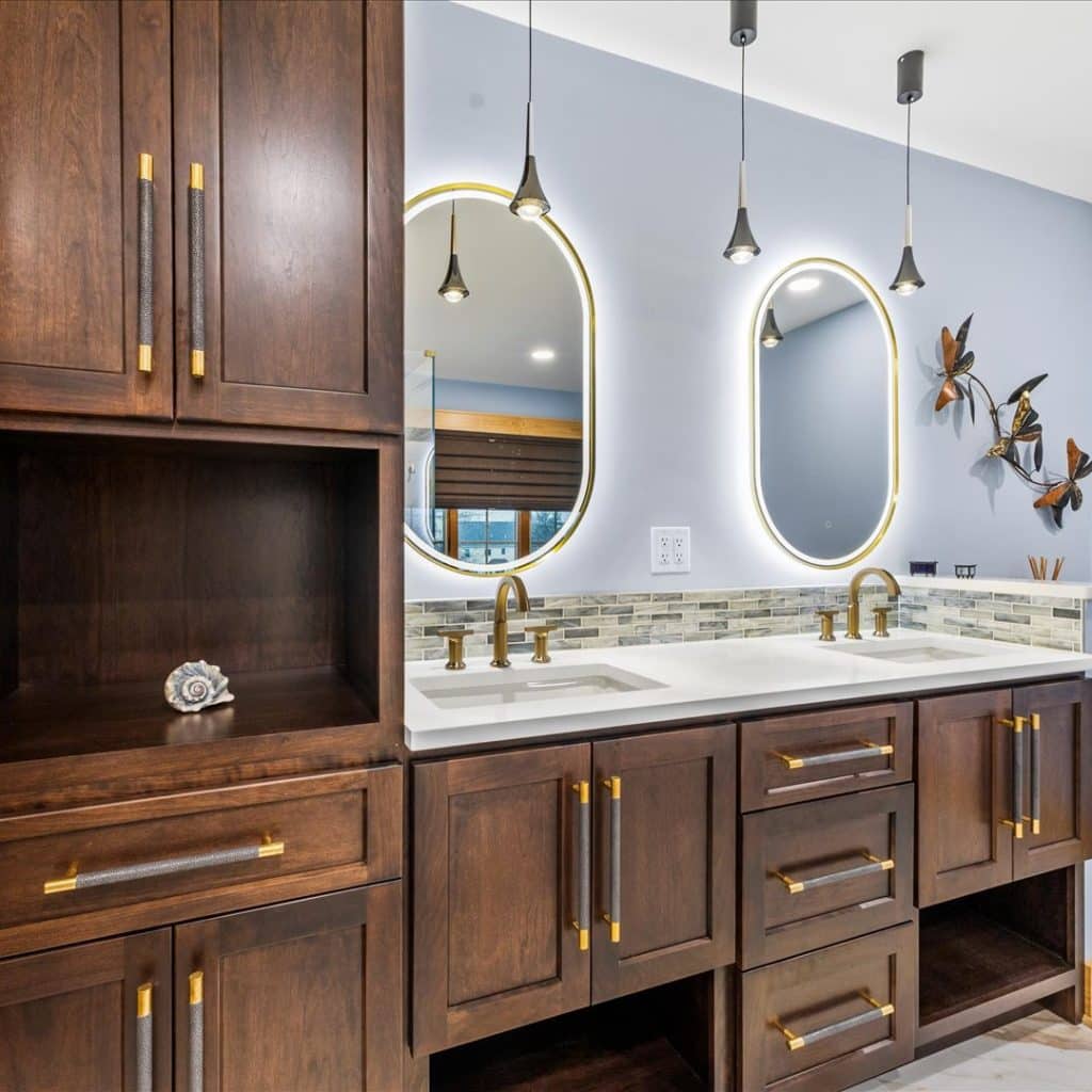 Bathroom Plumbing Fixtures in Milford NJ 1 bathroom with light blue walls, oval mirrors, dual sink, hanging light fixtures, wooden cabinets